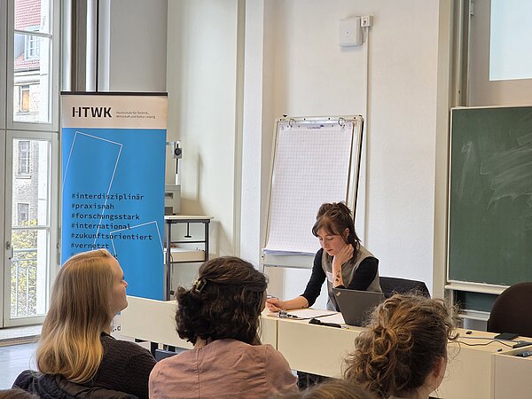 Pauline Seuß sitzt an einem Tisch und schaut auf ihre Notizen. Vor ihr sitzen drei Personen und hören zu.