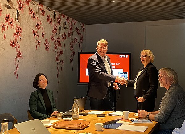 v.l.: Nicola Kopp-Rostek, Rainer Wilke Kasanický, Prof.in Swantje Rother, Wilfried Schumacher (Schatzmeister der DFTA). (Foto: DFTA) vier Personen in einem dunklen raum, zwei davon schüteln einander die Hände
