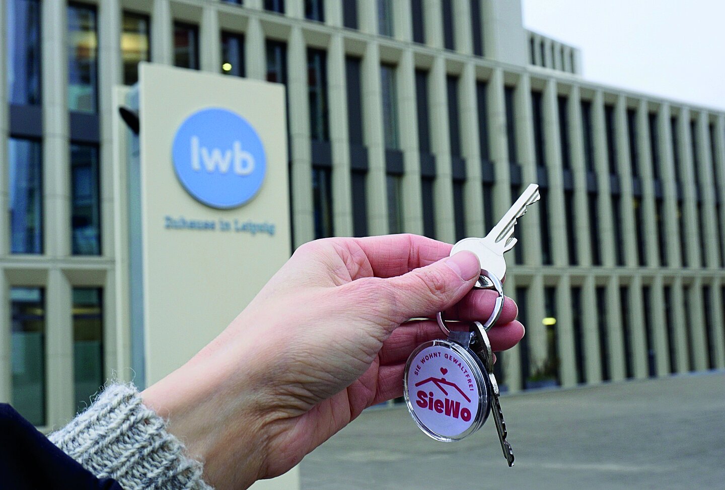 Hand mit einem Schlüssel vor einem Gebäude der LWB