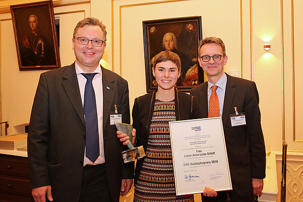 Esther Anna-Luise Ortloff steht zwischen dem Hauptgeschäftsführer des BME e.V. und Professor Michael Eßig von der Universität der Bundeswehr München. Esther hält eine Urkunde in der Hand.