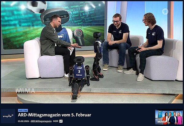 Felix Loos (re.) und Johannes Walter (mi.) von den HTWK Robots waren am 05.02.2026 mit zwei Robotern im "ARD-Mittagsmagazin" als Talkgäste zu Gast bei Tino Böttcher (li.). Im Fernsehstudio interagiert Moderator Tino Böttcher sichtlich begeistert mit einem der beiden HTWK Roboten im Gespräch mit Felix Loos und Johannes Walter.