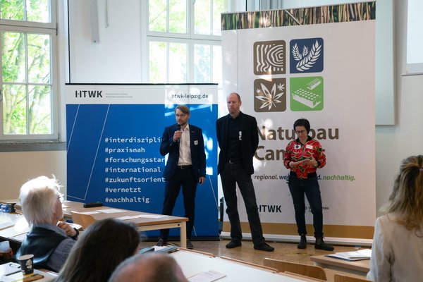 Nachhaltig Bauen und Sanieren 2026 3 Personen stehen vor großen Roll-ups und sprechen in ein Mikrofon
