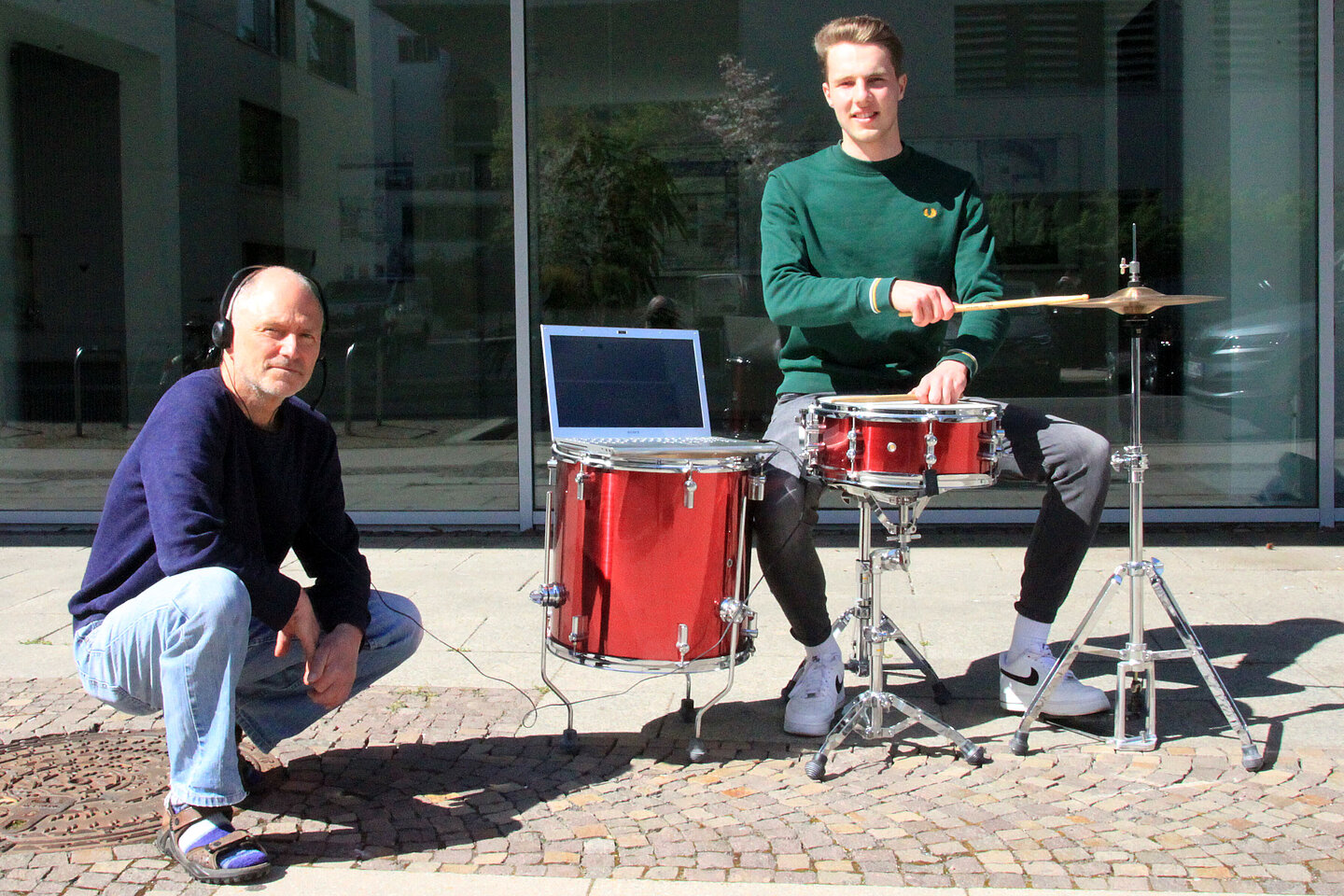Professor Christian Weickhardt und Florian Wedhorn (v.l., Foto: Marie Nowicki/HTWK Leipzig) In der Sonne steht ein rotes Schlagzeug, daran sitzt Florian Wedhorn und hält die Schlagzeugstöcke auf die Trommeln; auf einer der Trommeln steht ein Laptop und daneben hockt Professor Christian Weickhardt mit Kopfhörern
