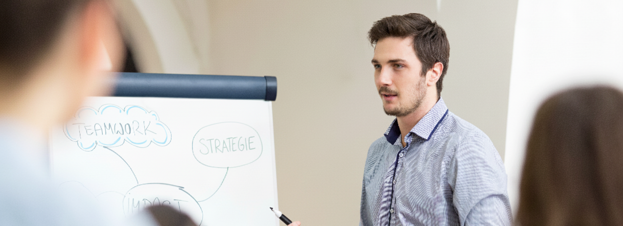 Ein Student erklärt anderen Studierenden etwas am Flipchart.