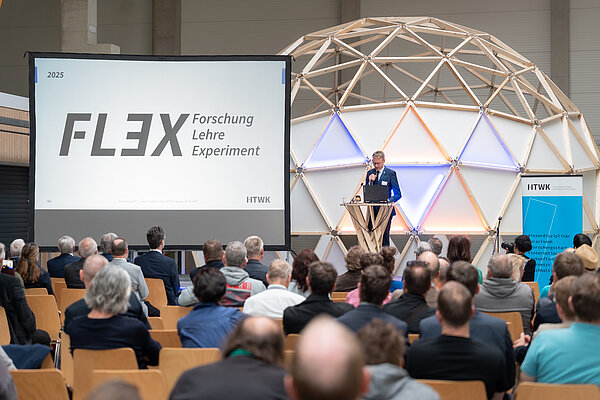 10 Jahre FLEX Ein Sprecher spricht vor sitzendem Publikum in einer Halle