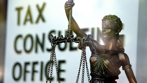 Illustration zum Fachgebiet: Bronzene Justitia vor Schriftwand "Tax Consulting Office"
