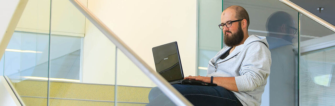 Ein Student mit Laptop sitzt auf einer Treppe.