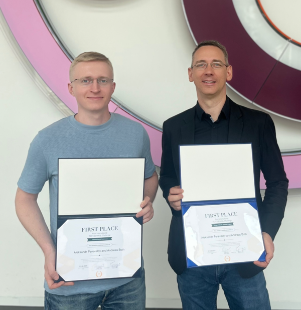 Aleksandr Perevalov (li.) und Prof. Dr. Andreas Both Zwei Männer mit Urkunden vor kreisförmigem Kunstwerk