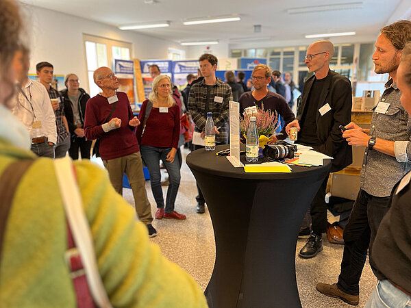 Menschen stehen um einen Tisch herum und sind im Gespräch.