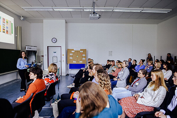 Professorin Graßmann steht vor dem Publikum und hält eine Keynote. Im Hintergrund auf der Wand ist ihre Powerpoint-Präsentation zu sehen.