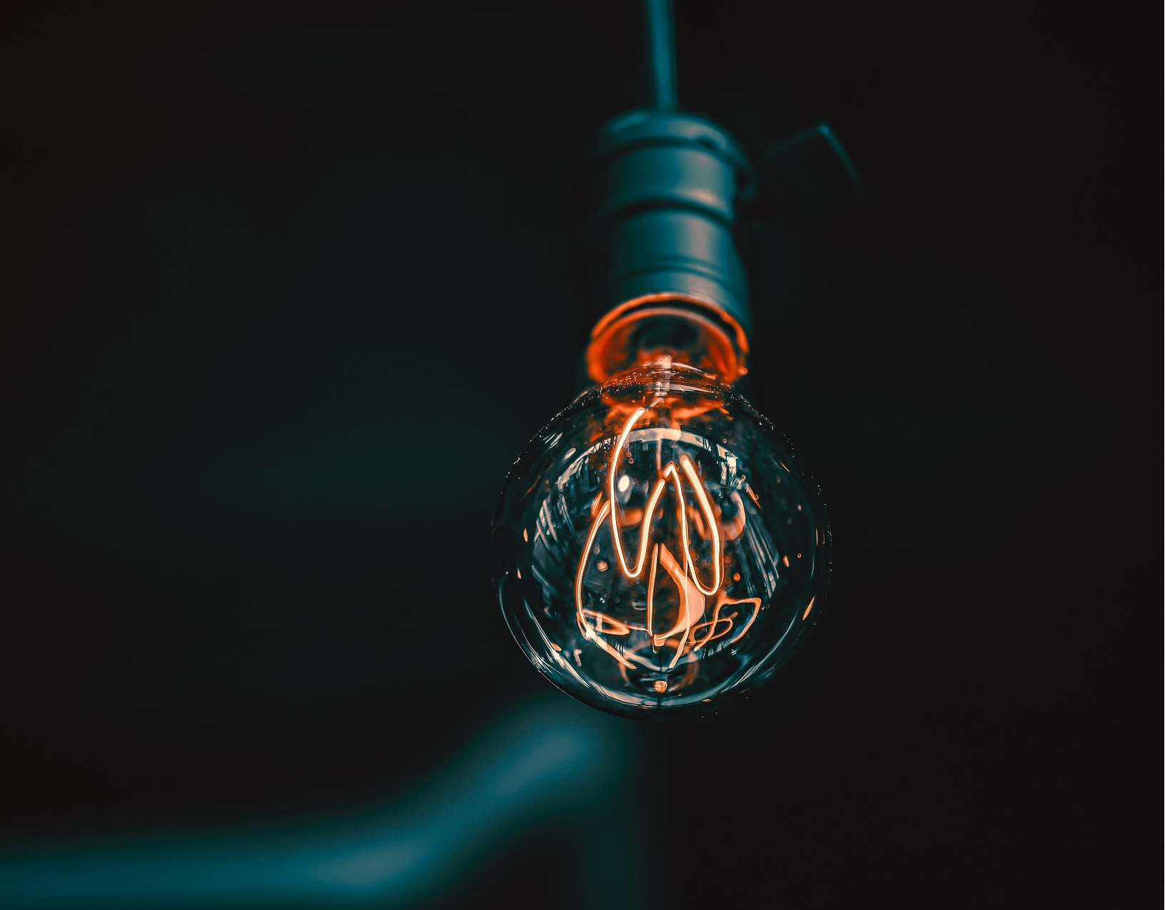 Eine schwarze Glühbirne mit einem sehr langen Leuchtdraht hängt vor einem schwarzen Hintergrund.