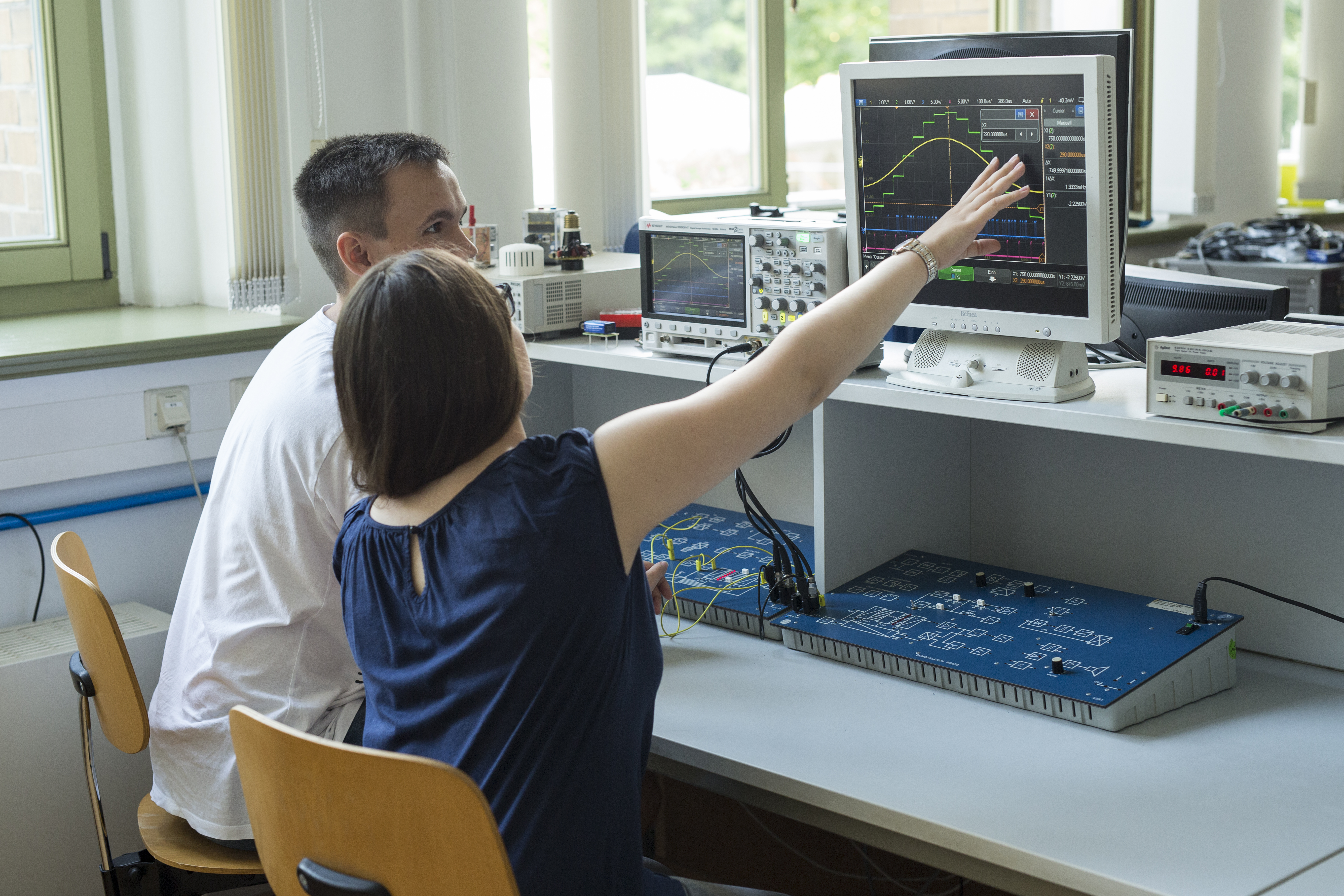Zwei Studenten sitzen im Labor vor einem Bildschirm, eine Studentin zeigt auf den Bildschirm. Darauf sieht man die Digitalisierung eines analogen Signals.