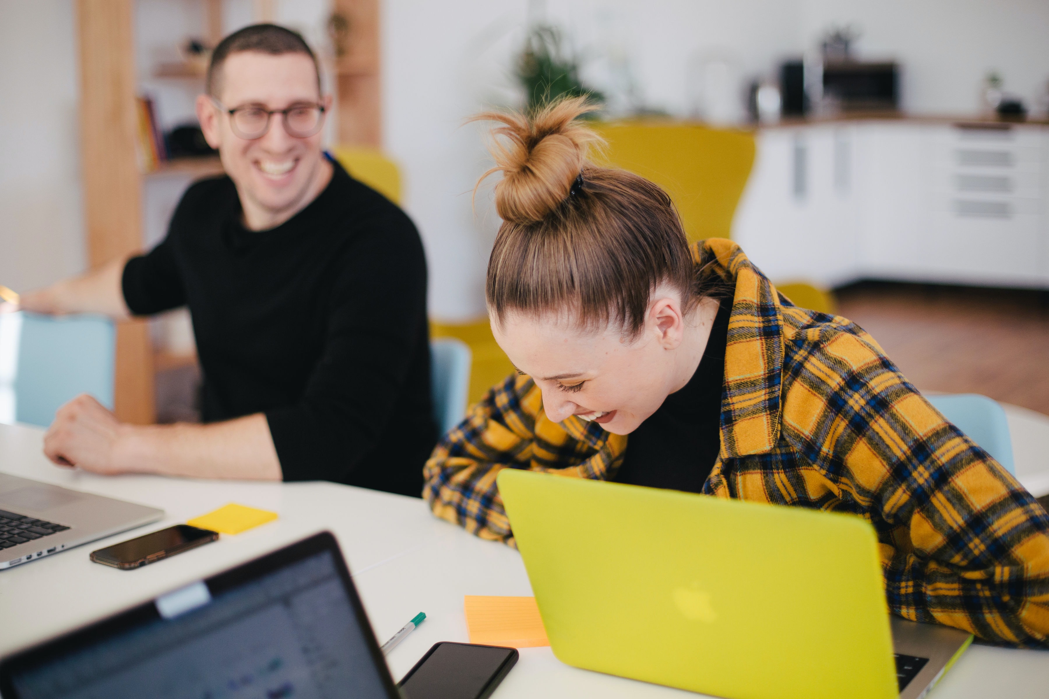 Generation Z Ein Mann und eine Frau sitzen gemeinsam am Schreibtisch und lachen.
